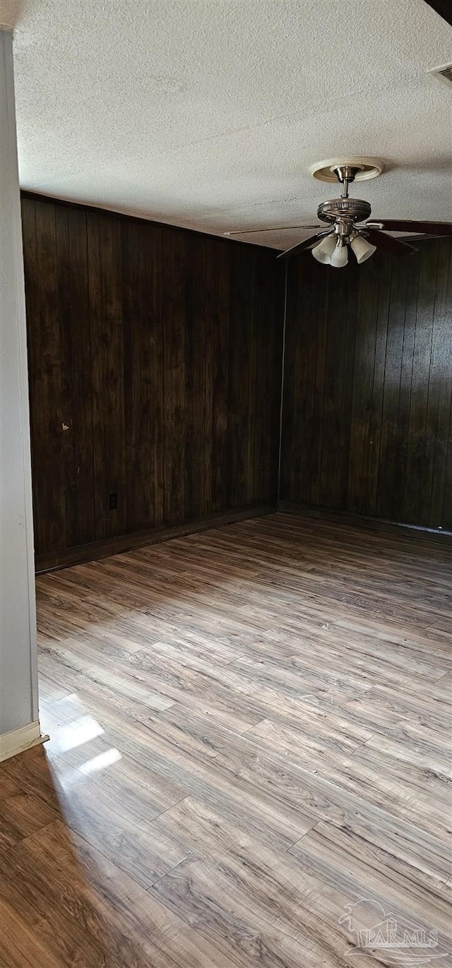 empty room featuring wood walls, ceiling fan, light hardwood / wood-style floors, and a textured ceiling