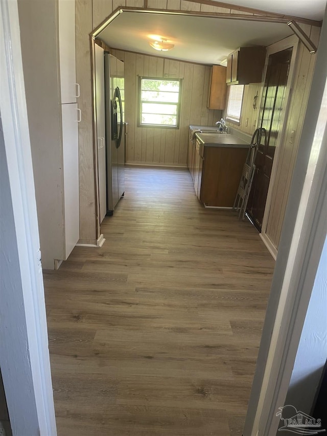kitchen with brown cabinets, wooden walls, light wood finished floors, and stainless steel fridge with ice dispenser