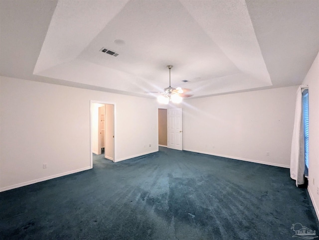 spare room with a tray ceiling, dark carpet, and ceiling fan