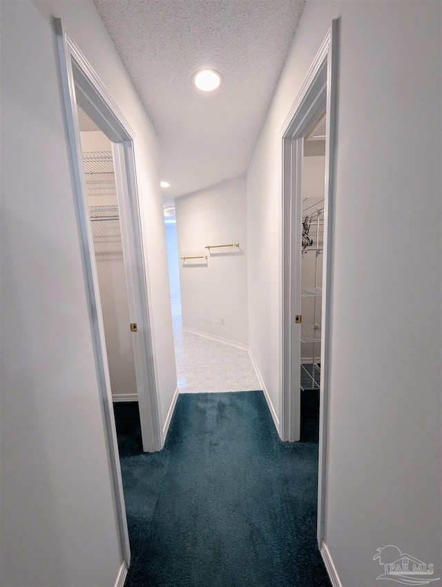 hall with a textured ceiling and dark colored carpet