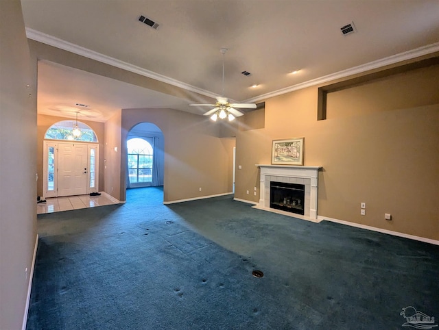 unfurnished living room featuring a tiled fireplace, crown molding, ceiling fan, and dark colored carpet