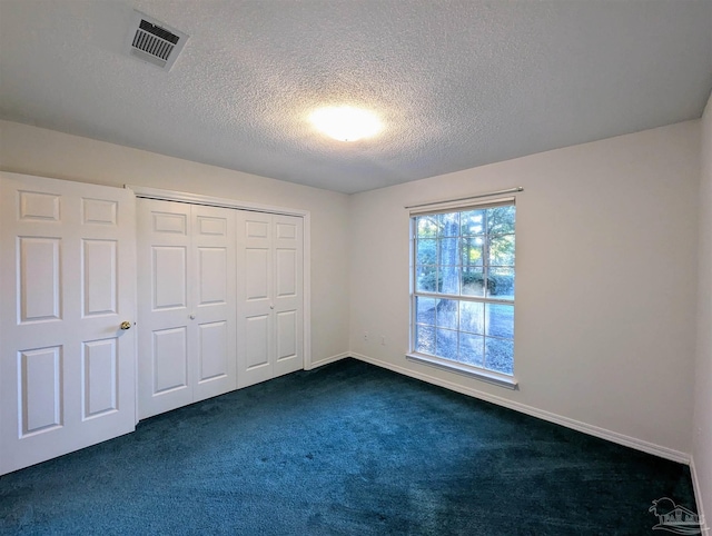 unfurnished bedroom featuring dark colored carpet, a textured ceiling, and a closet