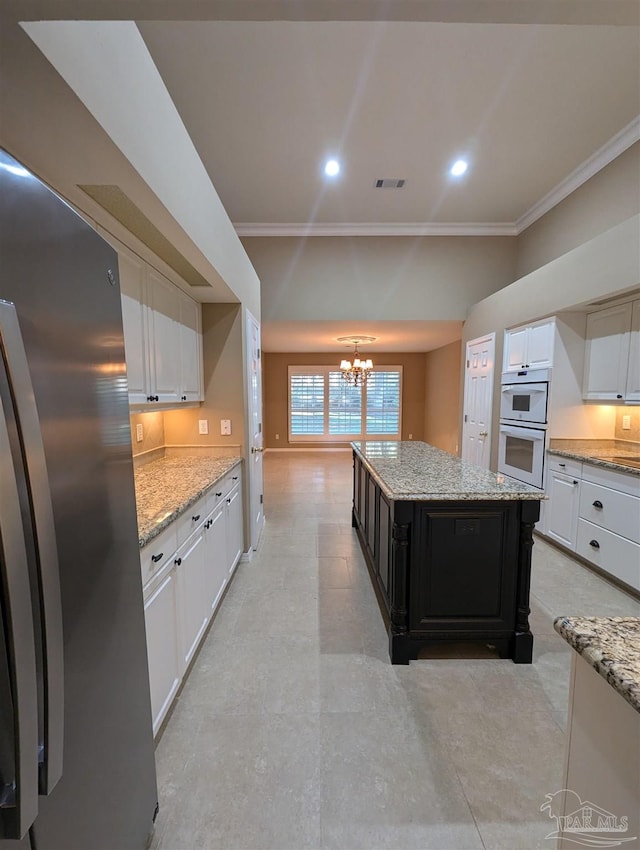 kitchen with stainless steel refrigerator, white cabinetry, a center island, and a chandelier