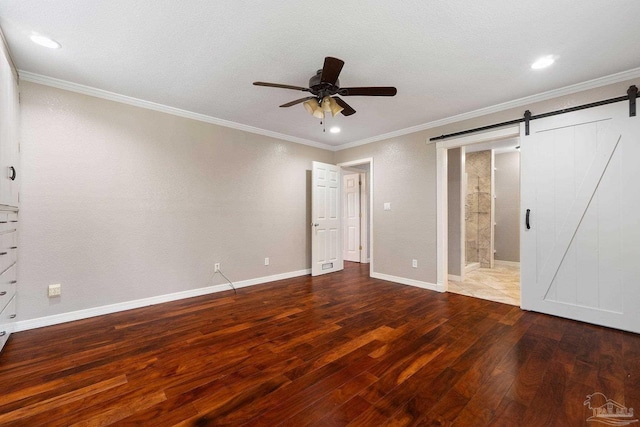 unfurnished bedroom with ensuite bathroom, ceiling fan, hardwood / wood-style flooring, a barn door, and ornamental molding