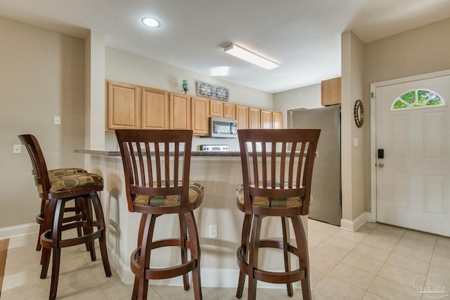 kitchen with a kitchen breakfast bar, kitchen peninsula, stainless steel appliances, and light brown cabinetry