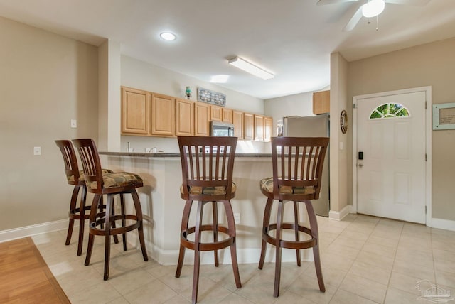 kitchen with ceiling fan, light brown cabinets, kitchen peninsula, a breakfast bar area, and light tile patterned floors