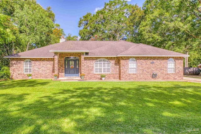 ranch-style home with a shingled roof, a front yard, brick siding, and a chimney