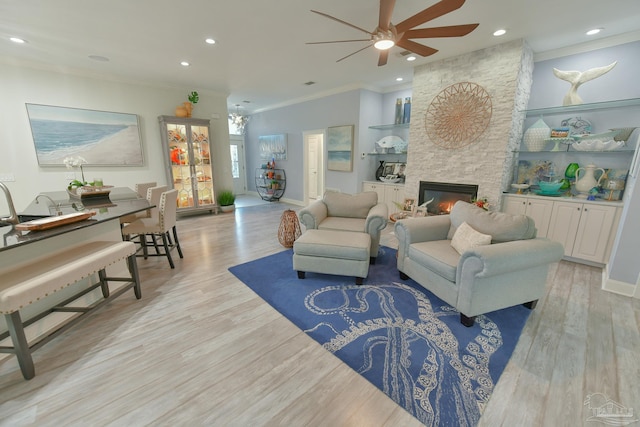 living room with ornamental molding, a stone fireplace, light wood-type flooring, and ceiling fan with notable chandelier
