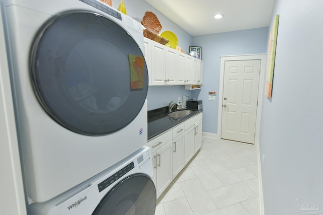laundry area featuring a sink, light tile patterned flooring, stacked washing maching and dryer, cabinet space, and baseboards