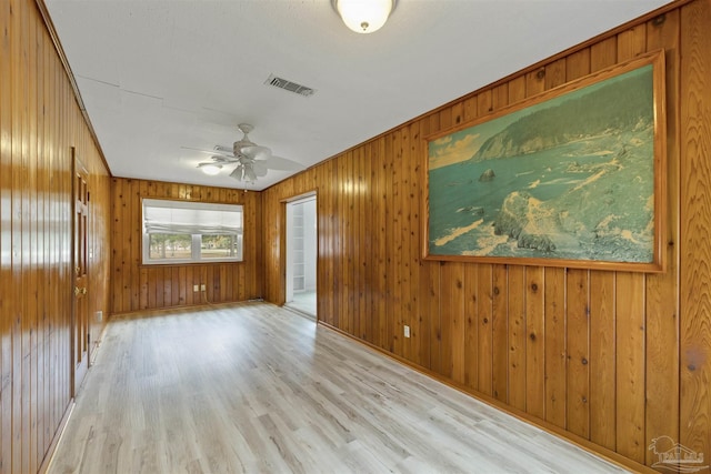 spare room featuring light hardwood / wood-style flooring, ceiling fan, and wood walls