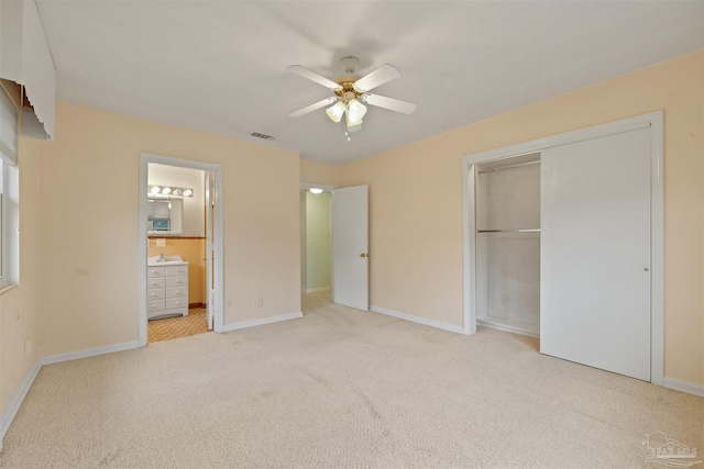 unfurnished bedroom featuring ensuite bathroom, ceiling fan, light colored carpet, and a closet