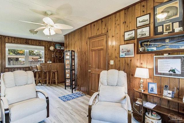 living room with wood walls, ceiling fan, and light hardwood / wood-style floors