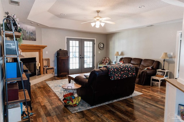 living room featuring french doors, a textured ceiling, a tray ceiling, dark hardwood / wood-style flooring, and a fireplace