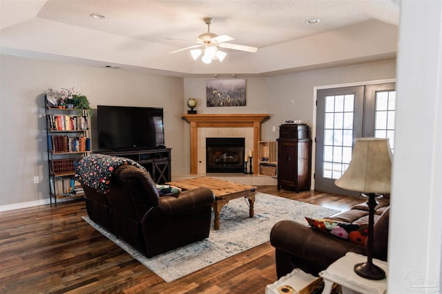 living room with dark hardwood / wood-style floors, a tiled fireplace, ceiling fan, a raised ceiling, and a textured ceiling