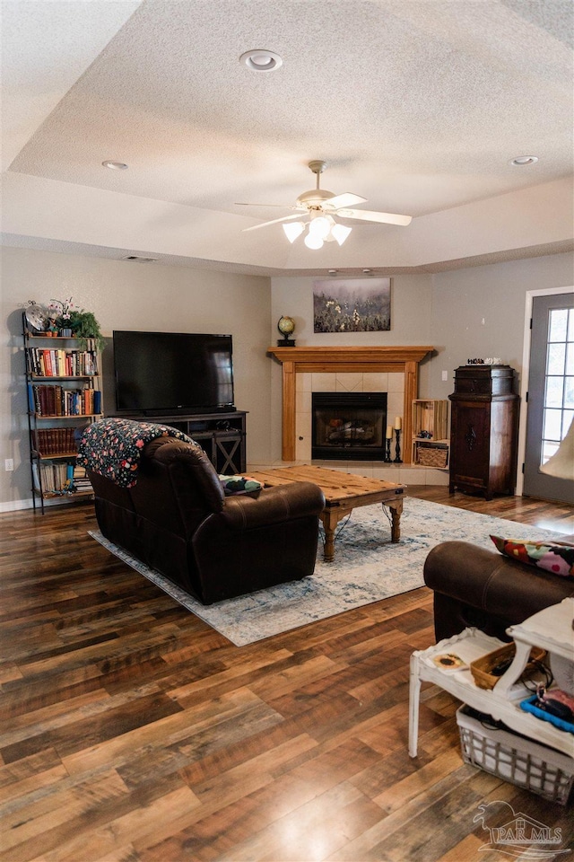 living room featuring a tiled fireplace, wood-type flooring, a textured ceiling, and ceiling fan