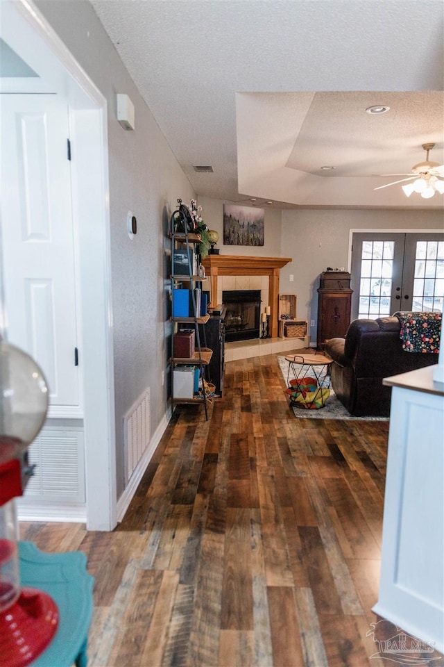 living room featuring french doors, a textured ceiling, dark hardwood / wood-style floors, a tile fireplace, and ceiling fan