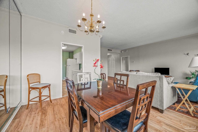 dining space with a textured ceiling, light wood finished floors, a chandelier, and visible vents