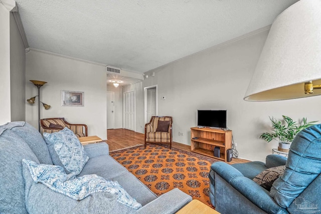 living area with crown molding, a textured ceiling, visible vents, and wood finished floors