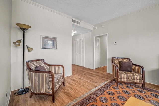 sitting room with a textured ceiling, ornamental molding, wood finished floors, and visible vents