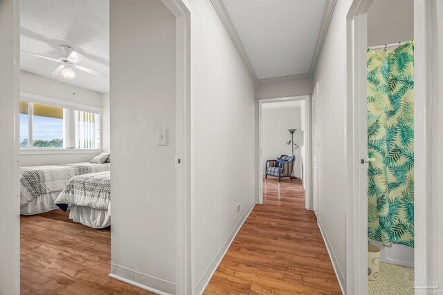 hall with light wood-type flooring, crown molding, and baseboards