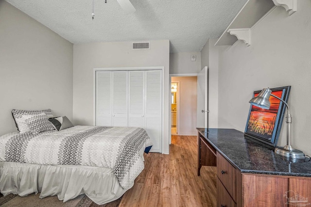 bedroom with a textured ceiling, ceiling fan, wood finished floors, visible vents, and a closet