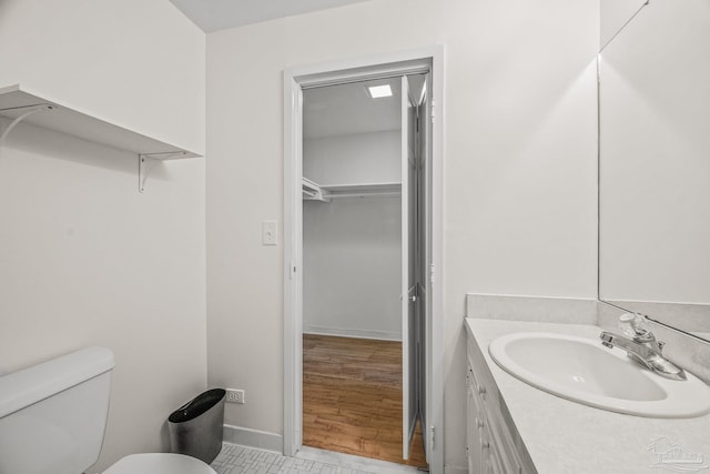 bathroom featuring toilet, a spacious closet, baseboards, and vanity