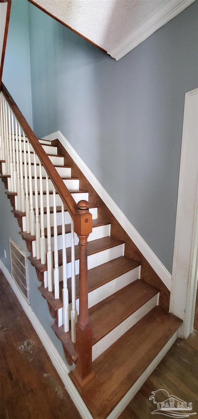 stairs featuring a textured ceiling, crown molding, and wood-type flooring