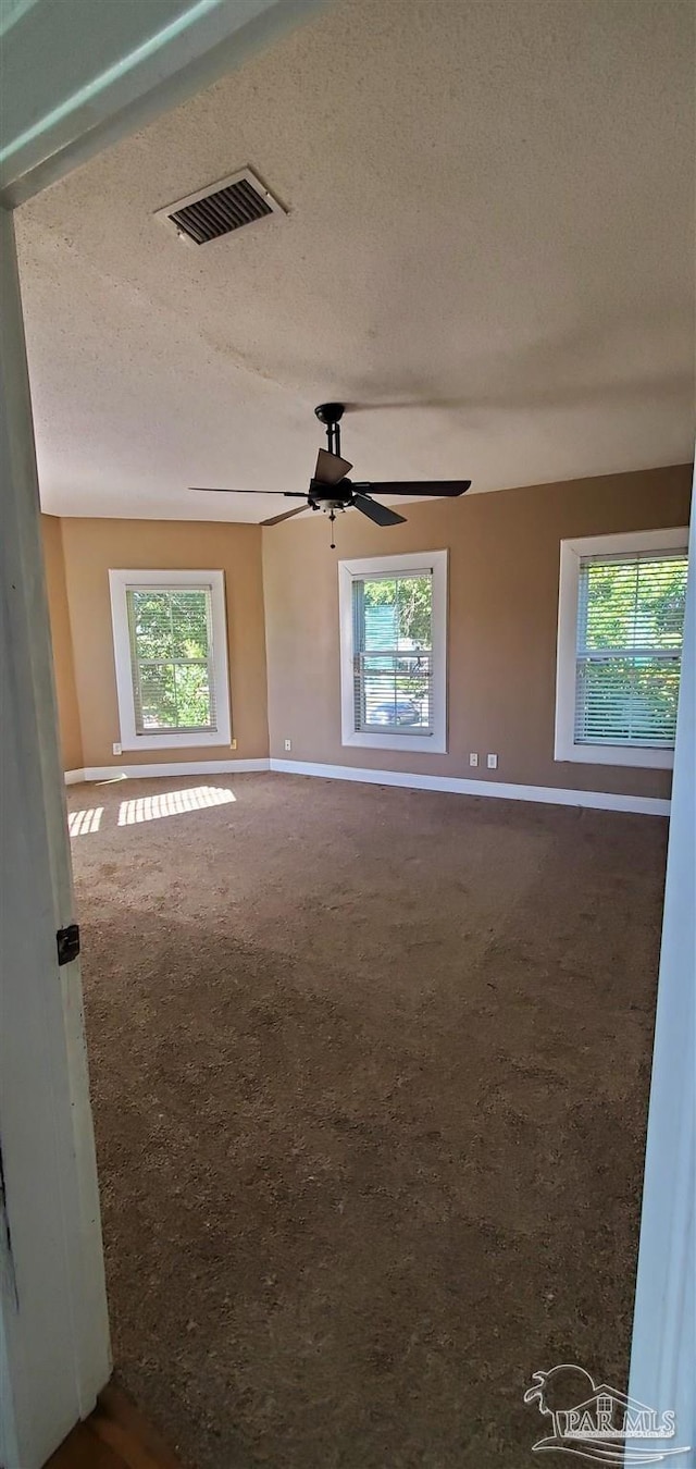 spare room featuring a textured ceiling, dark colored carpet, and ceiling fan