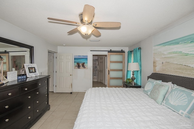 bedroom with visible vents, light tile patterned flooring, a barn door, connected bathroom, and a ceiling fan