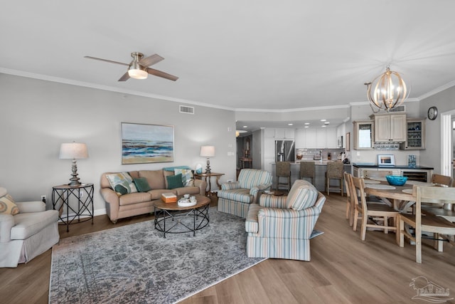 living room with ceiling fan with notable chandelier, light hardwood / wood-style flooring, and ornamental molding