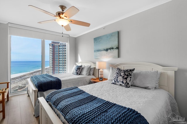 bedroom featuring ceiling fan, crown molding, a water view, a beach view, and light hardwood / wood-style flooring