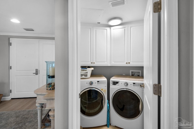 clothes washing area featuring light hardwood / wood-style floors, cabinets, and washing machine and clothes dryer