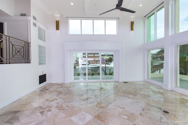 unfurnished living room with ceiling fan, a high ceiling, and plenty of natural light