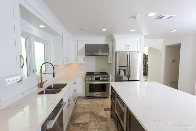 kitchen with light stone counters, sink, wall chimney range hood, and stainless steel appliances