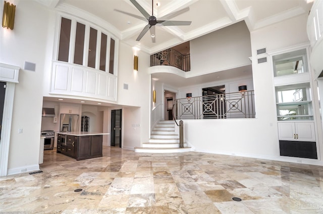 unfurnished living room with ceiling fan, ornamental molding, and a high ceiling