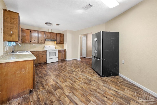 kitchen featuring decorative backsplash, white electric range oven, sink, dark hardwood / wood-style floors, and stainless steel refrigerator