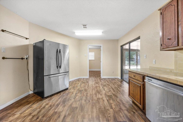 kitchen featuring appliances with stainless steel finishes, a textured ceiling, dark hardwood / wood-style floors, and tile counters