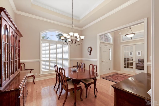 dining space with a raised ceiling, crown molding, light wood finished floors, and a chandelier