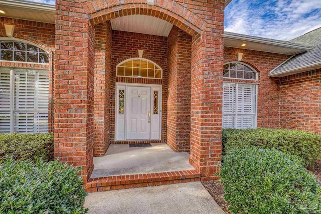 doorway to property with brick siding and a shingled roof