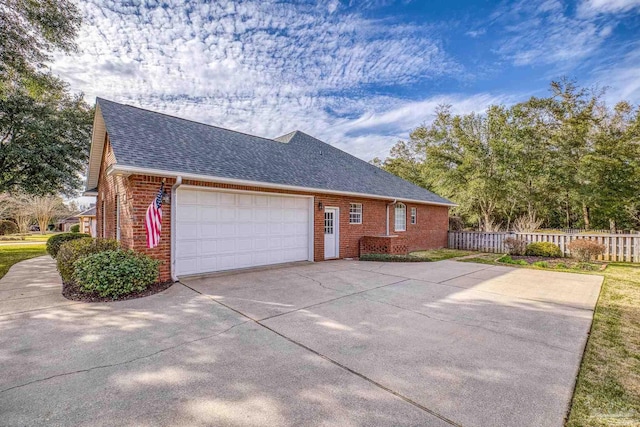 view of side of property with fence, driveway, an attached garage, a shingled roof, and brick siding