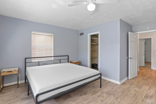 bedroom with a closet, wood-type flooring, a walk in closet, and ceiling fan