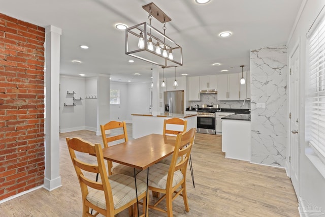 dining space with brick wall, sink, and light hardwood / wood-style flooring