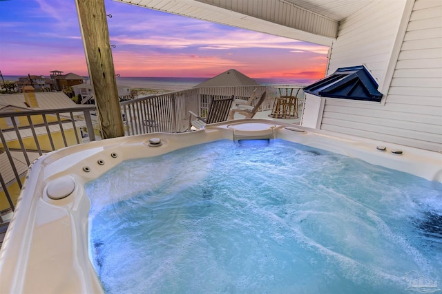 pool at dusk featuring a hot tub