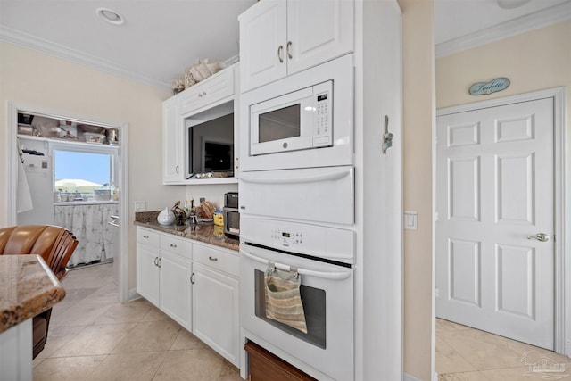 kitchen with white cabinets, dark stone counters, white appliances, light tile patterned floors, and ornamental molding