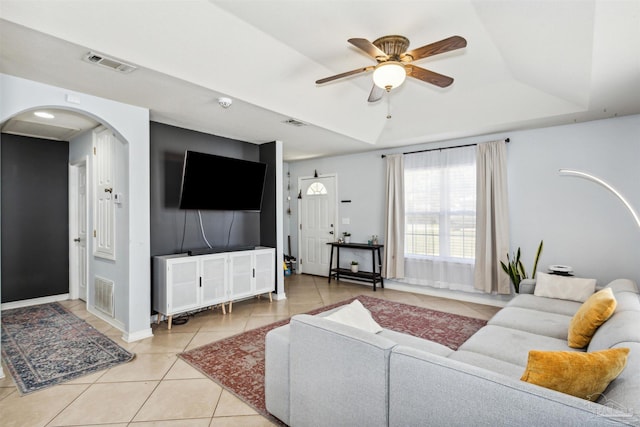 tiled living room with ceiling fan and a tray ceiling