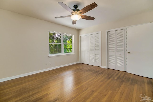 unfurnished bedroom featuring multiple closets, ceiling fan, and dark wood-type flooring