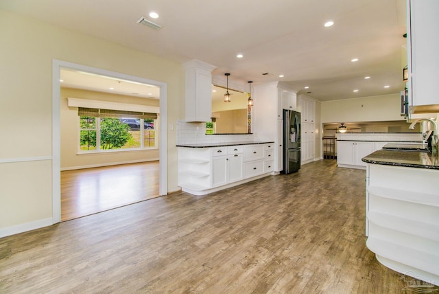 kitchen with stainless steel refrigerator with ice dispenser, sink, white cabinetry, hanging light fixtures, and light hardwood / wood-style flooring