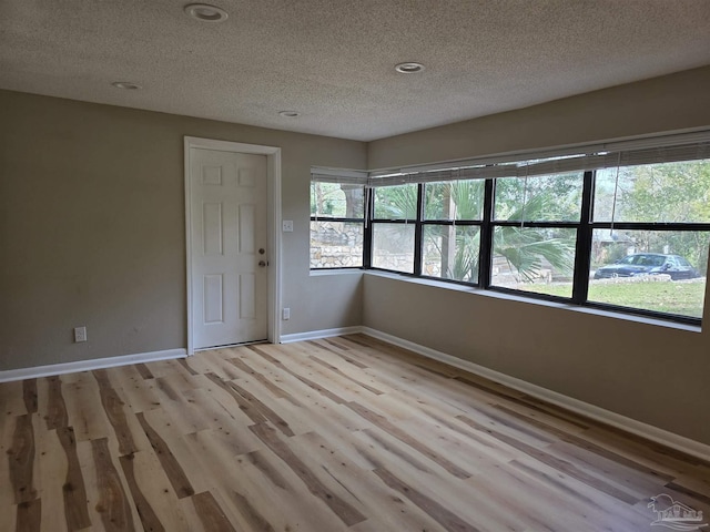 spare room with plenty of natural light, a textured ceiling, baseboards, and wood finished floors