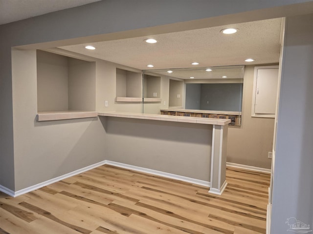 kitchen with a peninsula, light wood finished floors, tile counters, and a textured ceiling