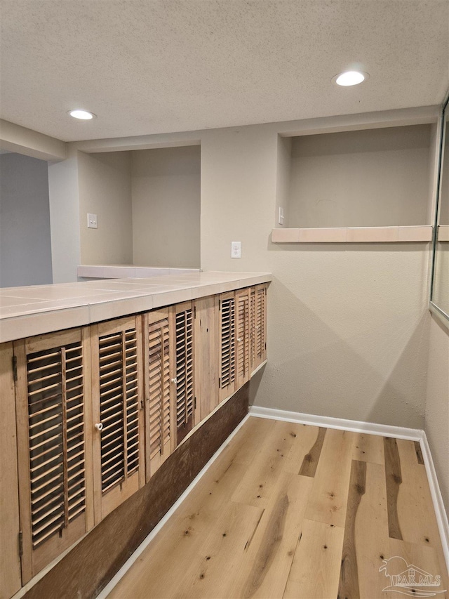 hall with a textured ceiling, baseboards, and wood finished floors